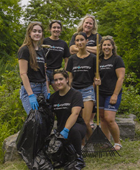 a group of young teenage girls from Enviroventure standing by some trees with a garbage bag and rake