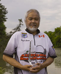 Herb Quan standing outdoors in front of a body of water holding his award